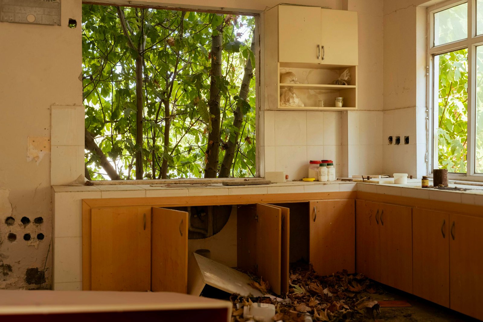 An old kitchen interior with broken cabinets and autumn leaves, revealing an abandoned atmosphere.