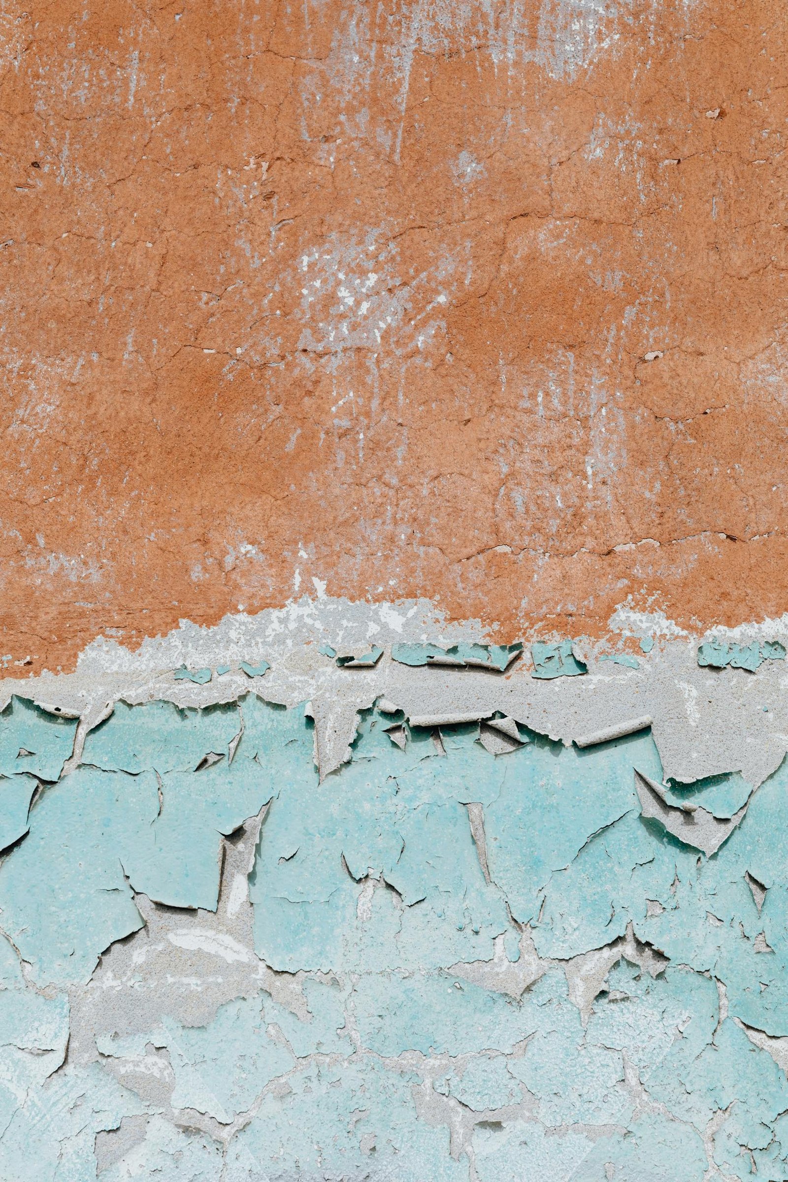 Close-up of a distressed wall with peeling paint and textured layers in blue and brown, showcasing urban decay.